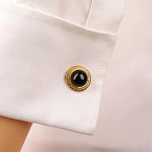 Macro shot of luxury gold-edged black resin cufflinks on white shirt sleeve cuff