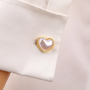 Eleganti gemelli a cuore dorati con inserto in perla su polsino di camicia bianca