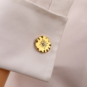 Macro detail of gold-plated cufflink with hammered texture and star-set crystal inlay