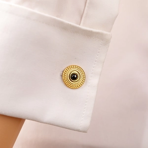Close-up of luxury gold-plated cufflinks with black center and beaded texture on white shirt
