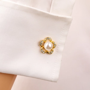 Macro di un gemello a forma di fiore dorato con perla e strass su un polsino di camicia