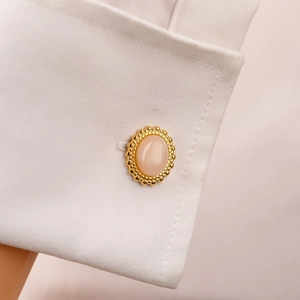 Detailed close-up of a golden oval cufflink with pink stone on a white shirt sleeve