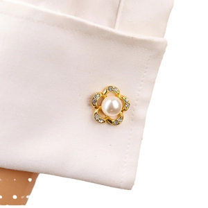 Gemelli a fiore dorati con perla e cristalli su polsino di camicia bianca