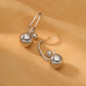 Detalle de los pendientes de doble esfera en plata pulida sobre fondo textil naranja