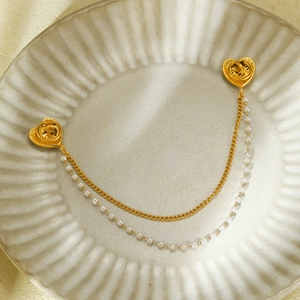 Dettaglio della spilla a cuore con catene dorate e perle su piatto in ceramica