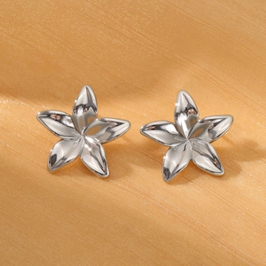 Primer plano de pendientes de flor frangipani en plata pulida sobre fondo de seda dorada