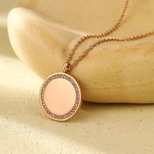 Détail d'un pendentif rond en or rose avec cristaux sur une surface en pierre naturelle