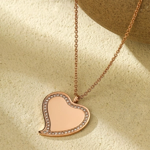 Détail du pendentif cœur en or rose avec bordure en cristal sur fond de sable