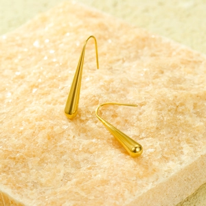 Détail de boucles d'oreilles gouttes dorées polies sur un présentoir en pierre