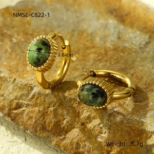 Detail van vintage gouden oorbellen met groene natuursteen op stenen achtergrond