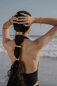 Polished 18K gold-plated hair accessories and jewelry on a model by the ocean