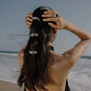 Three silver geometric hair rings styled on a sleek black ponytail with a coastal background