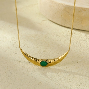 Detail van gouden maanvormige ketting met gehamerde textuur en groene edelsteen hanger