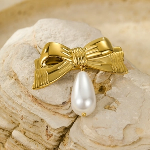 Elegant gold bow hair clip with white teardrop pearl pendant on a textured stone