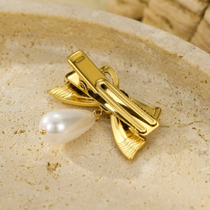 Golden bow hair clip with white teardrop pearl pendant on a natural stone tray
