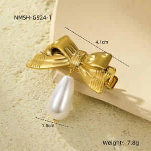Macro shot of a golden bow hair clip with a drop pearl pendant and detailed metal texture