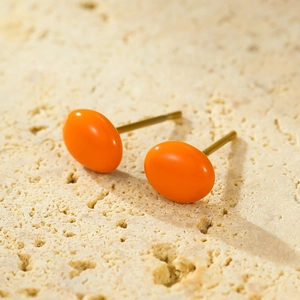 Macro shot of bright orange oval stud earrings on beige textured stone with gold plating