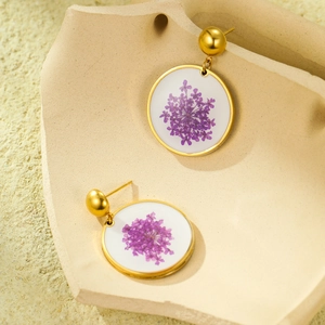 Detail of round gold titanium earrings featuring delicate pressed purple dried flowers