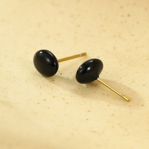 Macro shot of minimalist round gold stud earrings featuring polished black enamel stones