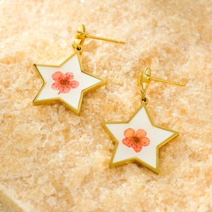 Macro detail of star-shaped earrings with real pink dried flowers and golden edges