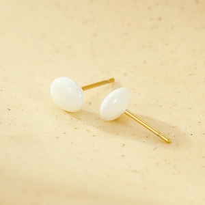 Close-up of minimalist white enamel stud earrings with 18K gold plated pin on stone surface