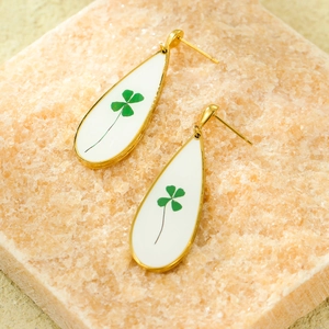 Golden teardrop earrings with white inlay and green four-leaf clover motif on crystal stone