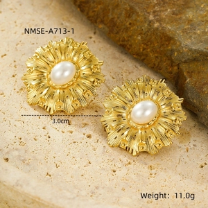Détail des boucles d'oreilles pétales dorées avec perle sur un support en pierre