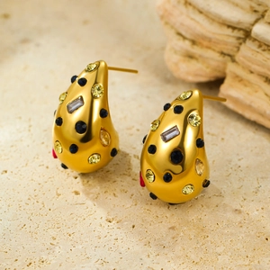Boucles d'oreilles goutte dorées avec zircons colorés sur un fond en pierre chaleureuse