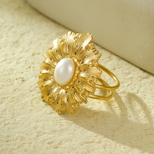 Close-up of golden sunflower ring with pearl inlay on sandy textured background