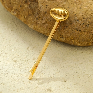 Détail d'une pince à cheveux coquillage dorée avec finition métallique sur une roche
