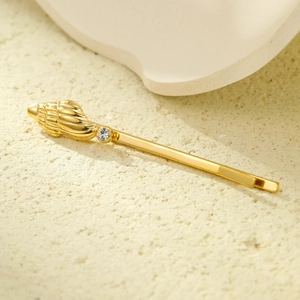 Détail d'une barrette coquillage dorée avec strass brillant sur un support de sable