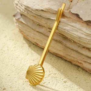 Détail d'une pince à cheveux coquillage dorée avec perle sur fond de roche