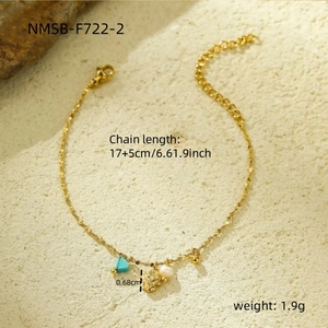 Detail van gouden kettingarmband met turquoise hart, parel en zonnehangers op textuurachtergrond