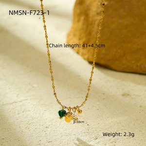 Detail van een gouden ketting met een groene hart hanger, parel en een reliëf munt