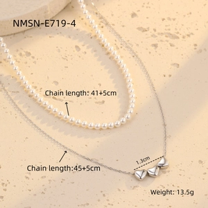 Detail van zilveren hartjesketting en parelchoker op een stenen ondergrond met afmetingen