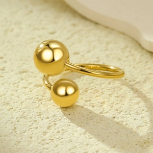 Bague ouverte dorée minimaliste avec sphères en métal poli sur surface en pierre