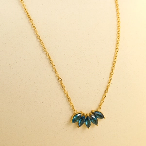 Dettaglio macro della collana dorata con ciondolo in zirconi blu scuro a forma di foglia