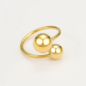 Vue macro d'une bague ouverte géométrique dorée avec deux billes en métal poli