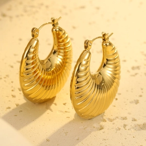 Close-up of gold hollow ribbed hoop earrings on a textured stone surface