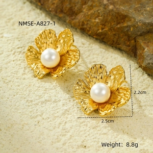Detalle macro de pendientes de pétalos bañados en oro 18k con perlas sobre fondo roca