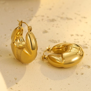 Detailed close-up of golden chunky twisted hoop earrings on a textured stone base