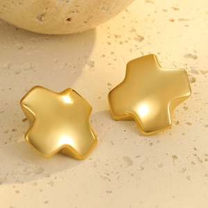 Makro-Detail von kreuzförmigen Ohrsteckern in mattem Gold-Finish auf Steinstruktur