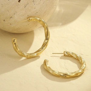 Détail de boucles d'oreilles dorées torsadées en C avec texture brossée sur un support
