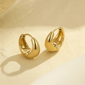 Polished chunky gold hoop earrings with minimalist design on natural stone surface