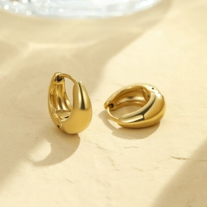 Close-up of chunky gold minimalist huggie hoop earrings with polished metal finish
