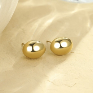 Gros plan de boucles d'oreilles haricot dorées avec finition miroir sur surface en pierre
