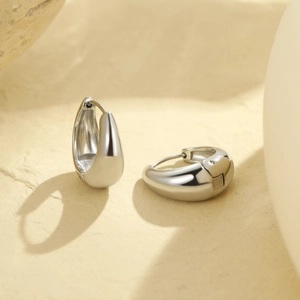 Macro shot of silver teardrop hoop earrings with high-polish finish on stone surface