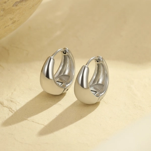 Polished silver stainless steel drop earrings shown on a textured stone surface