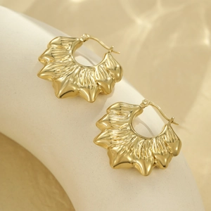 Détail de boucles d'oreilles dorées avec texture plissée sur support céramique