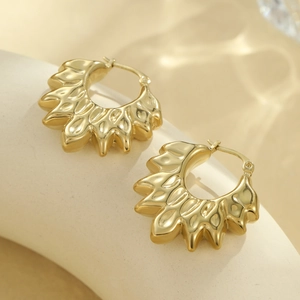 Gros plan de boucles d'oreilles dorées texturées sur un socle blanc au design minimaliste